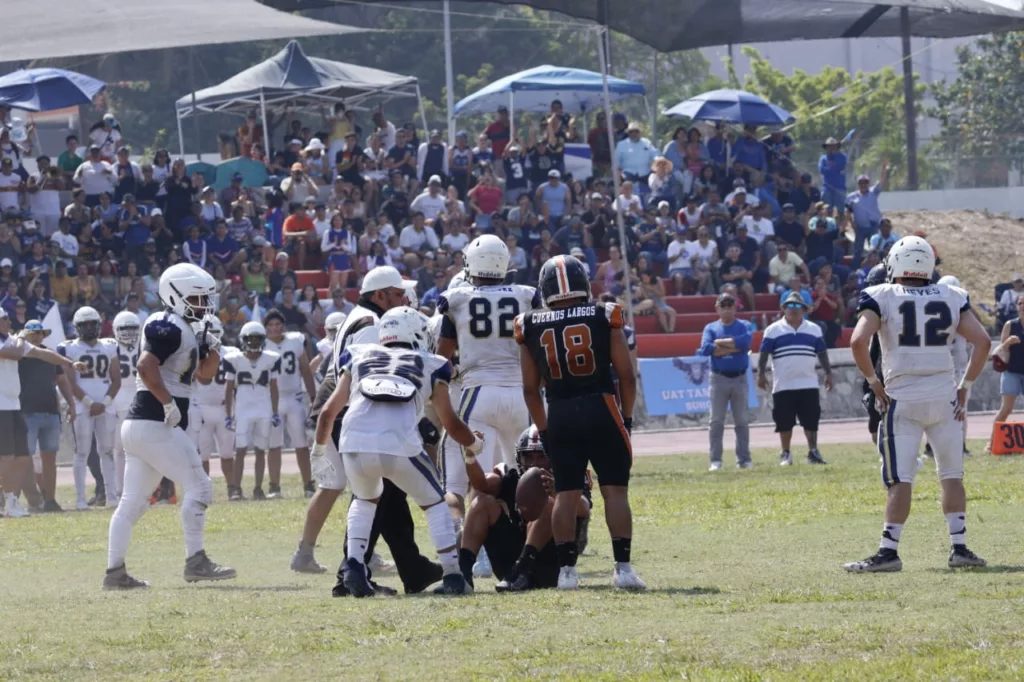 Victoria Decisiva en el Estadio Olímpico Los Cuernos Largos de la Facultad de Medicina Veterinaria y Zootecnia (FMVZ) se consagraron bicampeones de la Liga Universitaria de Fútbol Americano de la Universidad Autónoma de Tamaulipas (LUFAUAT) tras derrotar 6-0 a los Búhos de la Facultad de Derecho y Ciencias Sociales de Tampico (FADYCS). Encuentro Bajo el Sol Intenso El partido, que tuvo lugar el sábado 11 de mayo en el Centro Universitario Sur de Tampico, se desarrolló bajo un calor abrasador de más de 35 grados Celsius, con una destacada asistencia de aficionados que llenaron las gradas del estadio. Ceremonia de Premiación El rector de la UAT, MVZ Dámaso Leonardo Anaya Alvarado, junto con el secretario de Vinculación, MVZ Rogelio de Jesús Ramírez Flores, y los directores de las facultades FADYCS y FMVZ, estuvo presente para premiar a los bicampeones y subcampeones. Momentos Clave del Partido La única anotación del juego vino de Diego Alvarado, quien marcó el touchdown decisivo en el primer cuarto con una jugada terrestre de una yarda. Los Búhos estuvieron cerca de cambiar el destino del juego en el último cuarto, pero un fumble del quarterback Alejandro Pumarejo Díaz de León en los momentos críticos selló su suerte. Presencia y Apoyo del Rector El rector Anaya, que también realizó el lanzamiento de la moneda al inicio del partido, reiteró en su mensaje la importancia del deporte en su administración y agradeció a los padres de familia por su confianza en el proyecto educativo y deportivo de la universidad. Adicionalmente, anunció que la UAT participará nuevamente en la Liga Mayor de la ONEFA con el equipo Correcaminos, integrado por muchos jugadores de la final.