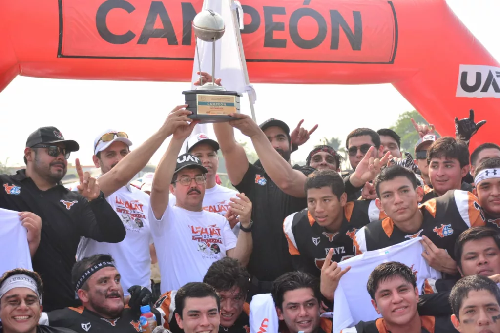 Victoria Decisiva en el Estadio Olímpico Los Cuernos Largos de la Facultad de Medicina Veterinaria y Zootecnia (FMVZ) se consagraron bicampeones de la Liga Universitaria de Fútbol Americano de la Universidad Autónoma de Tamaulipas (LUFAUAT) tras derrotar 6-0 a los Búhos de la Facultad de Derecho y Ciencias Sociales de Tampico (FADYCS). Encuentro Bajo el Sol Intenso El partido, que tuvo lugar el sábado 11 de mayo en el Centro Universitario Sur de Tampico, se desarrolló bajo un calor abrasador de más de 35 grados Celsius, con una destacada asistencia de aficionados que llenaron las gradas del estadio. Ceremonia de Premiación El rector de la UAT, MVZ Dámaso Leonardo Anaya Alvarado, junto con el secretario de Vinculación, MVZ Rogelio de Jesús Ramírez Flores, y los directores de las facultades FADYCS y FMVZ, estuvo presente para premiar a los bicampeones y subcampeones. Momentos Clave del Partido La única anotación del juego vino de Diego Alvarado, quien marcó el touchdown decisivo en el primer cuarto con una jugada terrestre de una yarda. Los Búhos estuvieron cerca de cambiar el destino del juego en el último cuarto, pero un fumble del quarterback Alejandro Pumarejo Díaz de León en los momentos críticos selló su suerte. Presencia y Apoyo del Rector El rector Anaya, que también realizó el lanzamiento de la moneda al inicio del partido, reiteró en su mensaje la importancia del deporte en su administración y agradeció a los padres de familia por su confianza en el proyecto educativo y deportivo de la universidad. Adicionalmente, anunció que la UAT participará nuevamente en la Liga Mayor de la ONEFA con el equipo Correcaminos, integrado por muchos jugadores de la final.